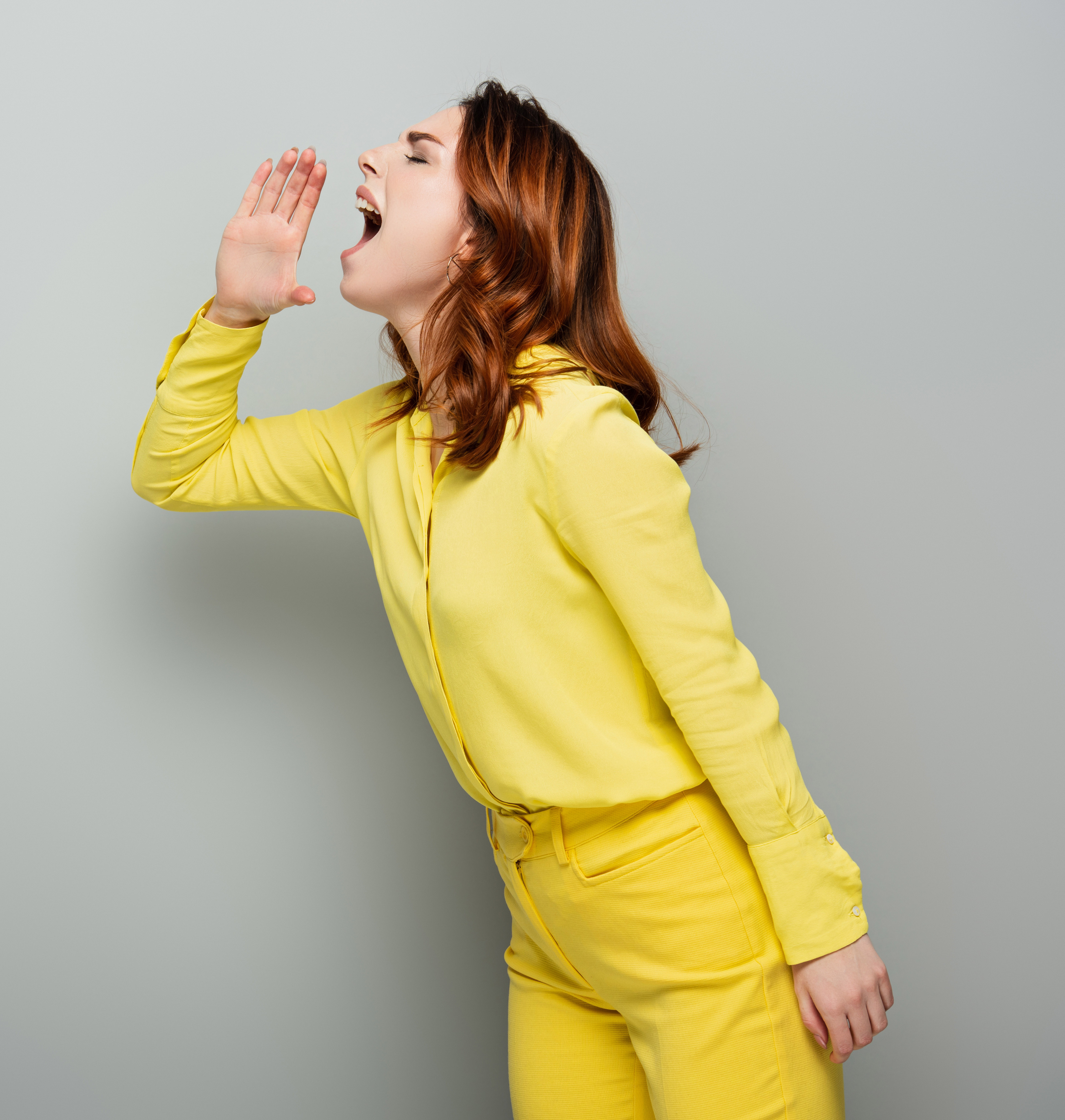 young woman in yellow clothes screaming while standing with closed eyes on grey